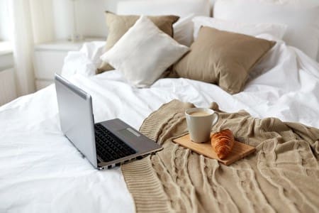 68094645 - coziness, technology, interior and winter concept - cozy bedroom with laptop computer, coffee cup and croissant on bed at home